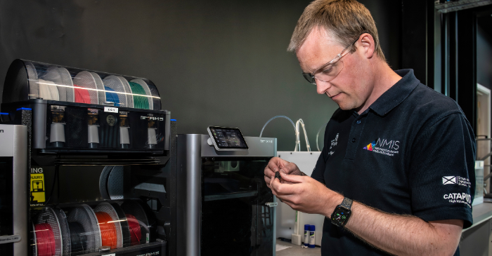 NMIS engineer inspecting an additively manufactured part infront of a desktop 3D printer